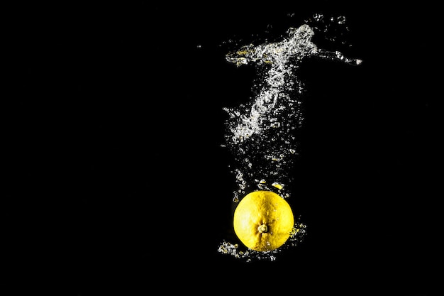 Lemon drop in water black background.