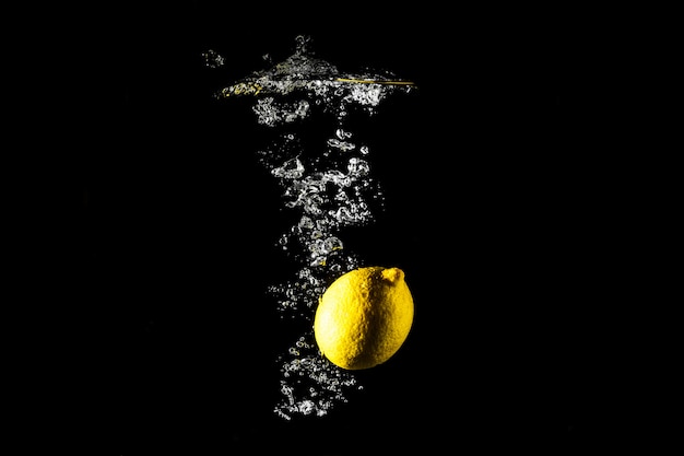 Lemon drop in water black background.