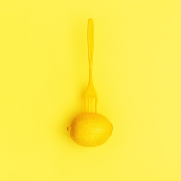 Lemon and fork on pastel yellow surface