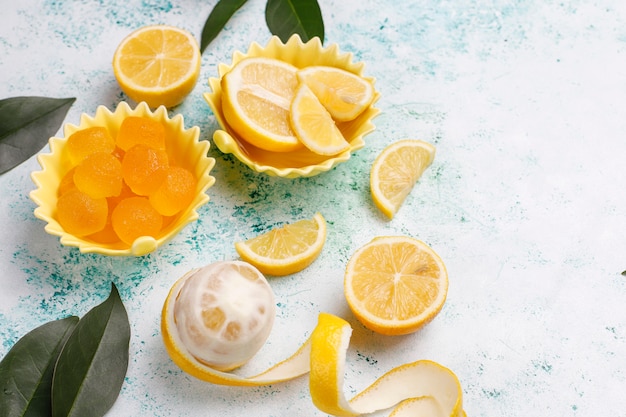 Lemon jelly candies with fresh lemons on concrete, top view