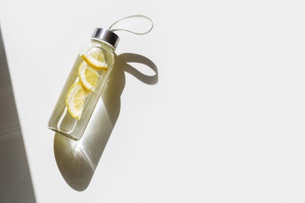 Lemon water drink detox in bottle hard shadow at sunlight on white background Wellness diet eating