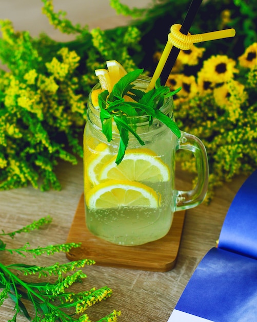 Lemon water,  lemonade in mugs with handles,  mason jar on a white wooden table.