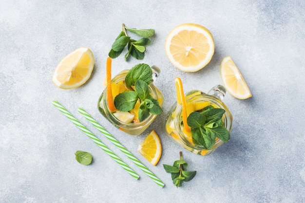 Lemonade drink of soda water, lemon and mint leaves in jar on light background.