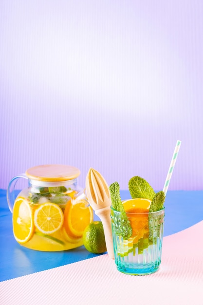 Lemonade drink of water, lemon, orange and mint leaves on multicolored background