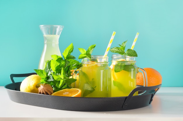 Lemonade in mason jar with lemon, orange and mint on blue. Copy space.