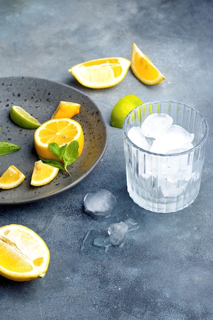 Lemonade preparationu glass with ice cubes fresh ingredients lemon and mint on gray ceramic plate