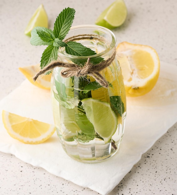 Lemonade in a transparent glass with lemon lime rosemary sprigs and mint leaves on a white background