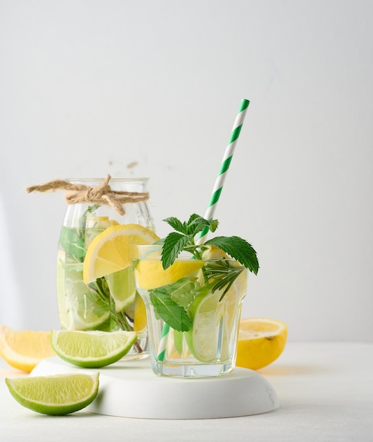 Lemonade in a transparent glass with lemon lime rosemary sprigs and mint leaves on a white background