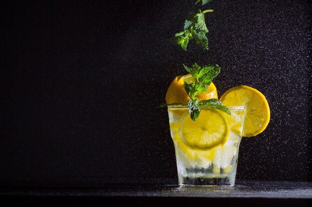 Lemonade with flying mint and lemon Summer refreshing drink with lemon on dark background