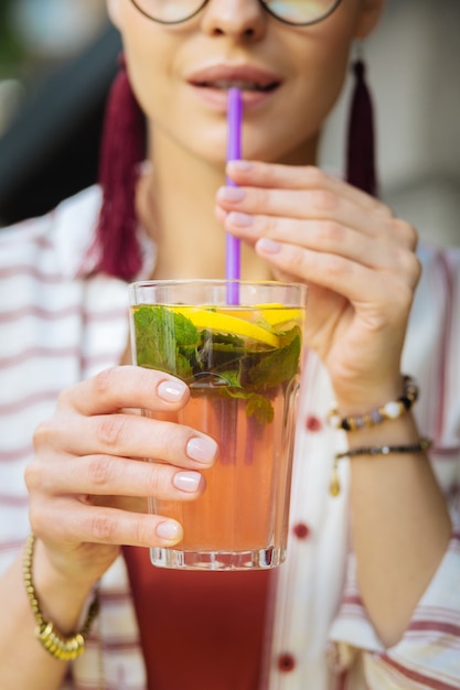 Lemonade with straw. Calm relaxed person sitting with a glass of cold lemonade and drinking it with a help of a sipping straw