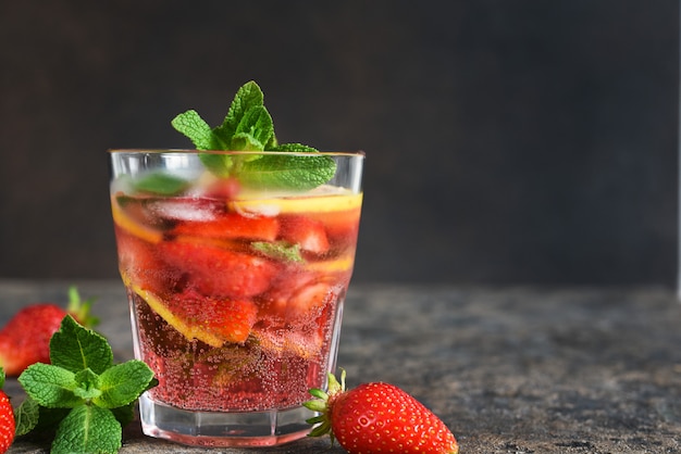 Lemonade with strawberries and mint on a dark concrete table.