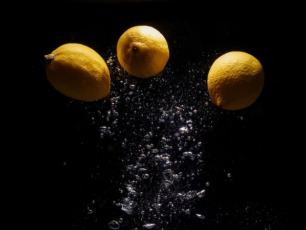 Lemons falling in water with splash on black background