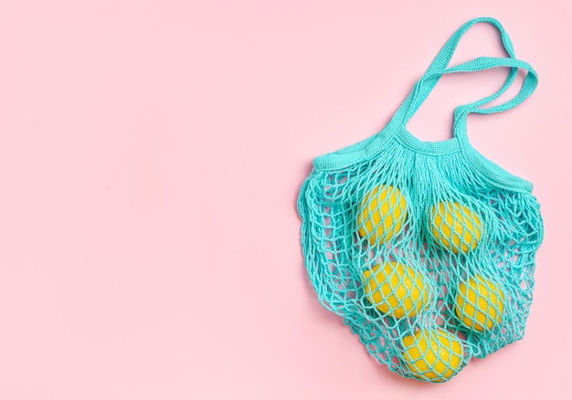 Lemons in mesh bag on pink background Zero waste shopping concept