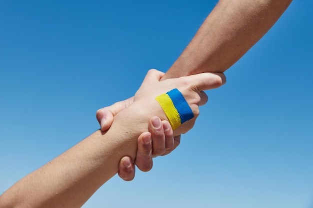 Lend a hand help painted in ukrainian flag colors against blue sky stand with ukraine