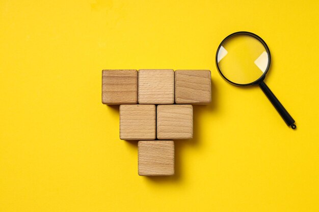 Lens and wooden cubes on yellow background space for text