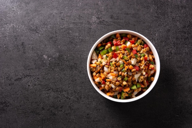 Lentil salad with peppersonion and carrot in a bowl on black slate background