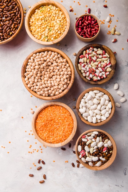 Lentils, chikpea and beans assortment in different bowls on white stone  table top view.