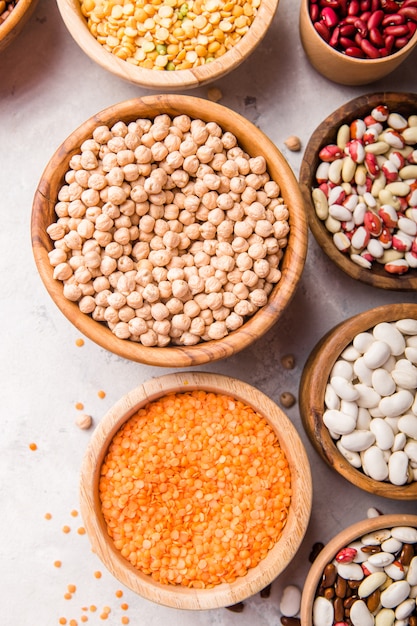 Lentils, chikpea and beans assortment in different bowls on white stone  table .