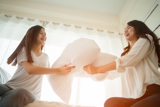 Lesbian women at pillow fights in bedroom.