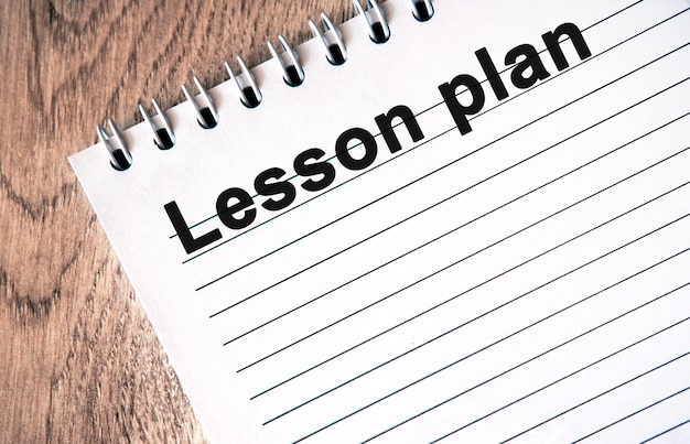 Photo lesson plan - black text on a white notebook with lines on a wooden table