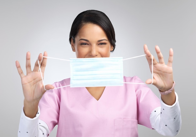 Let me help you Cropped portrait of an attractive young female healthcare worker holding up a mask in studio against a grey background