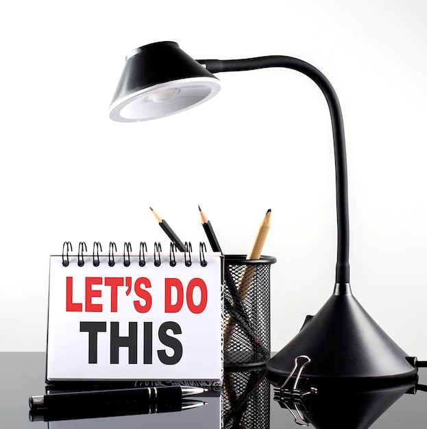 LET'S DO THIS text on notebook with pen and table lamp on the black background