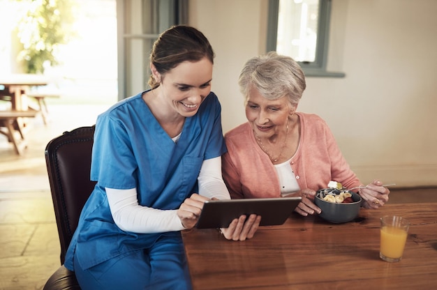 Lets tell the world how lovely it is here Shot of a young nurse and senior woman using a digital tablet at breakfast time in a nursing home