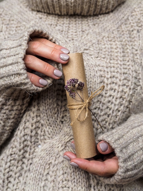 A letter decorated with a flower of oregano in the hands of a girl. a girl in a wool sweater holds a letter made of Kraft paper. Pre-holiday atmosphere