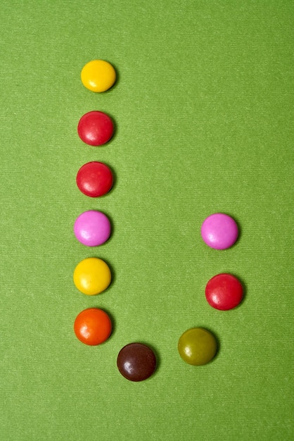 Letter J written with colored round chocolate candies on green background.