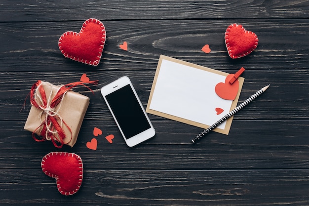 A letter of love, decorative paper hearts, gifts and smartphone on a dark table