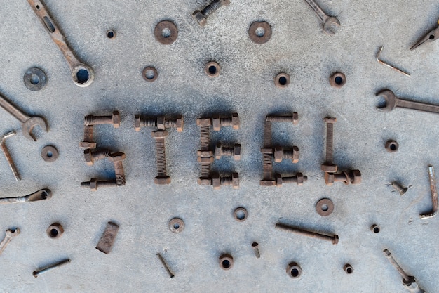 Letter word is steel by old and rusty nut on dirty ground