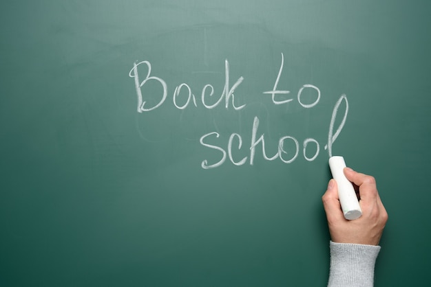 Lettering back to school in white chalk on a green chalk board, concept of the beginning of the school year