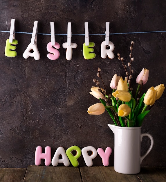 Photo lettering from cookies happy easter and bouquet tulips on stone background.