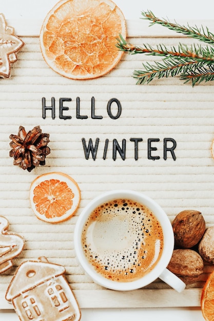 Lettering hello winter on letter board fir branches dried oranges nuts and a cup of coffee minimalis