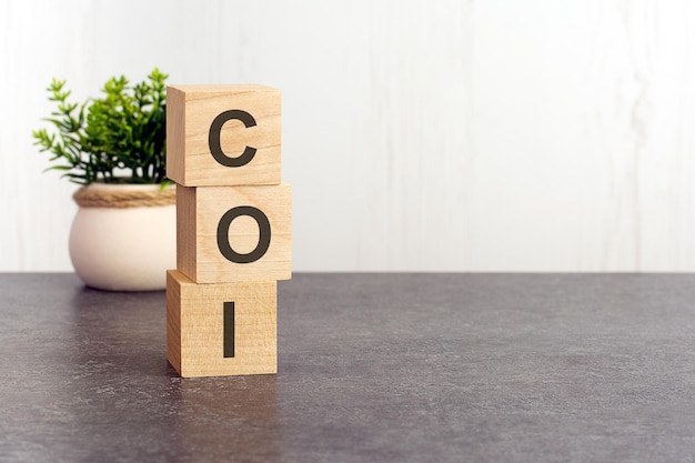 Letters of the alphabet of COI on wooden cubes green plant on a white background COI  short for Cost of Illness