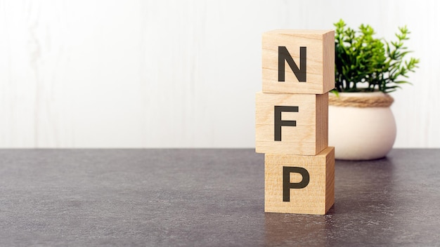 Letters of the alphabet of NFP on wooden cubes green plant white background NFP short for NonFarm Payroll