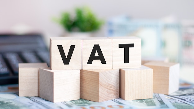 The letters VAT on wood cubes, banknotes and calculator on the background. VAT - short for value added tax. Business concept.