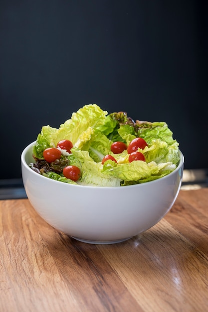 Lettuce salad and cherry tomatoes in white bowl on wooden table