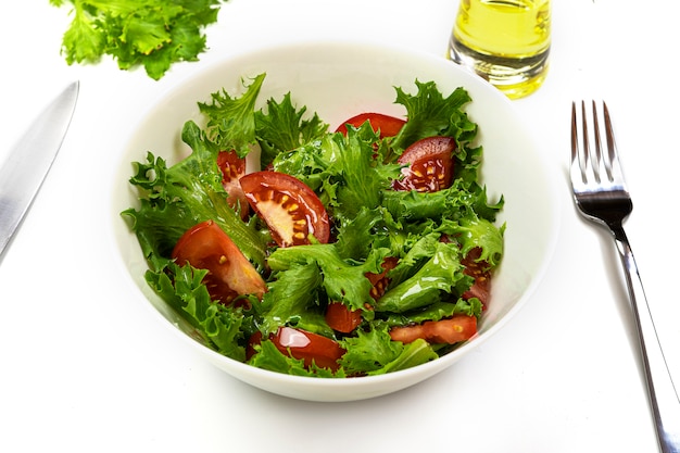 Lettuce and tomato salad with olive oil in a white deep dish. Healthy food.