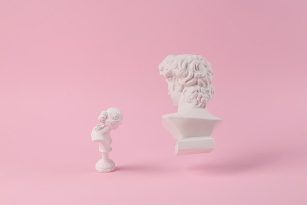 Levitating Antique Plaster busts of David and Venus on pink background with shadow Conceptual pop Minimal still life photography