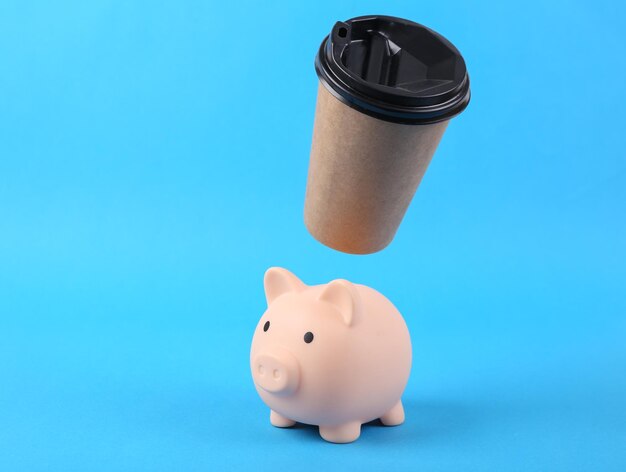 Levitating craft coffee cup with biggy bank on blue background