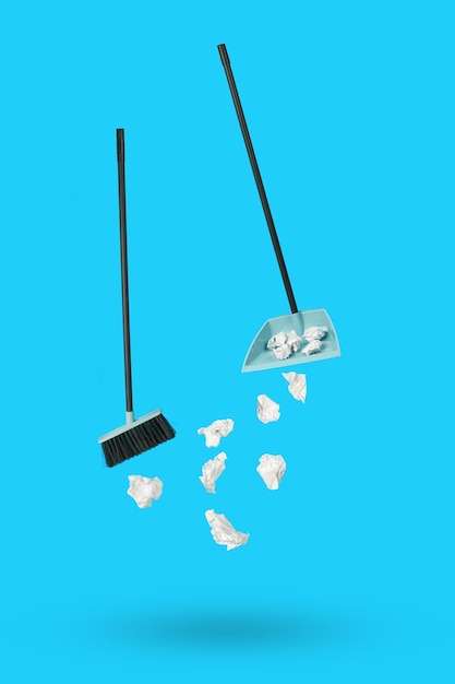 Levitating dustpan paper and cleaning brush on a blue background