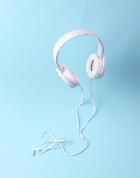 Levitating white cable stereo headphones on blue background