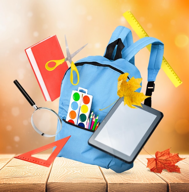 levitation of backpack and school supplies on wooden table and autumn background