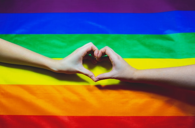 Lgbt community colorful flag. Two women's hands on rainbow background. Lesbian and gay problems. Legalization of marriage for couples with homosexual orientation.