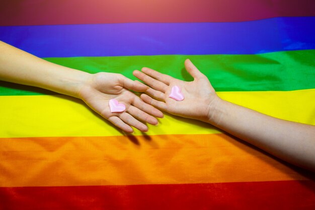 Lgbt community colorful flag. Two women's hands on rainbow background. Lesbian and gay problems. Legalization of marriage for couples with homosexual orientation.