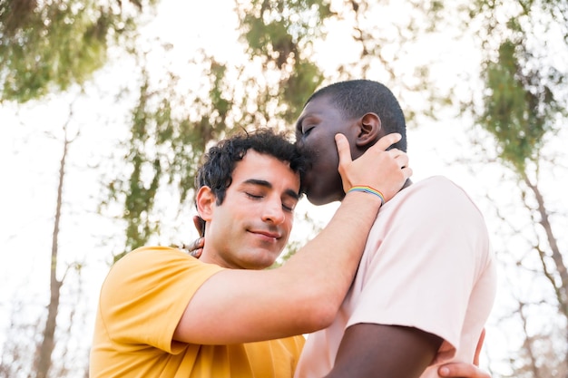 Lgbt concept couple of multiethnic men in a park kissing each other on the forehead romantic pose