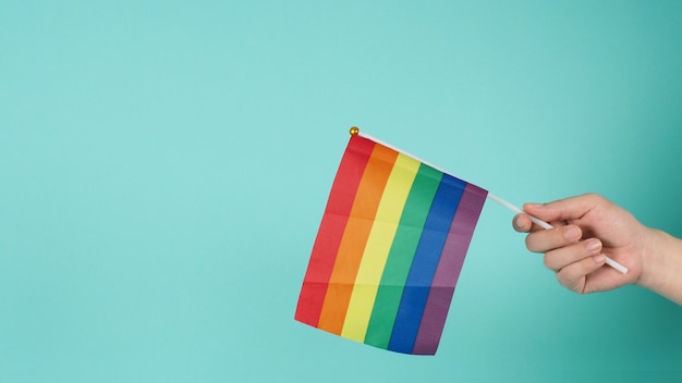 LGBT concept.Hand is holding a rainbow flag on mint green or tiffany blue background.