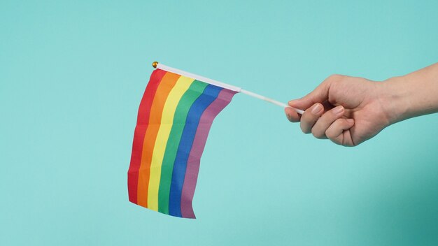 LGBT concept.Hand is holding a rainbow flag on mint green or tiffany blue background.