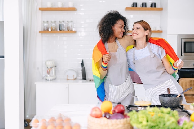 LGBT couple women happy celebrate pride month together with rainbow flag in kitchen cooking at home